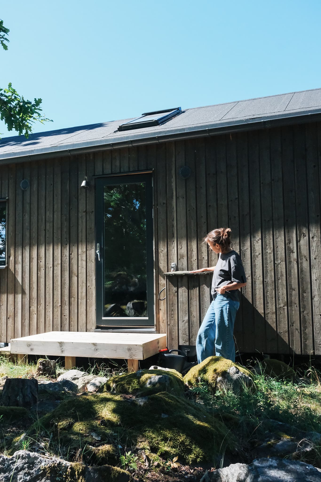 Kvinna vid yttre komposttoalettinstallation på mörk trästuga med svart tank under